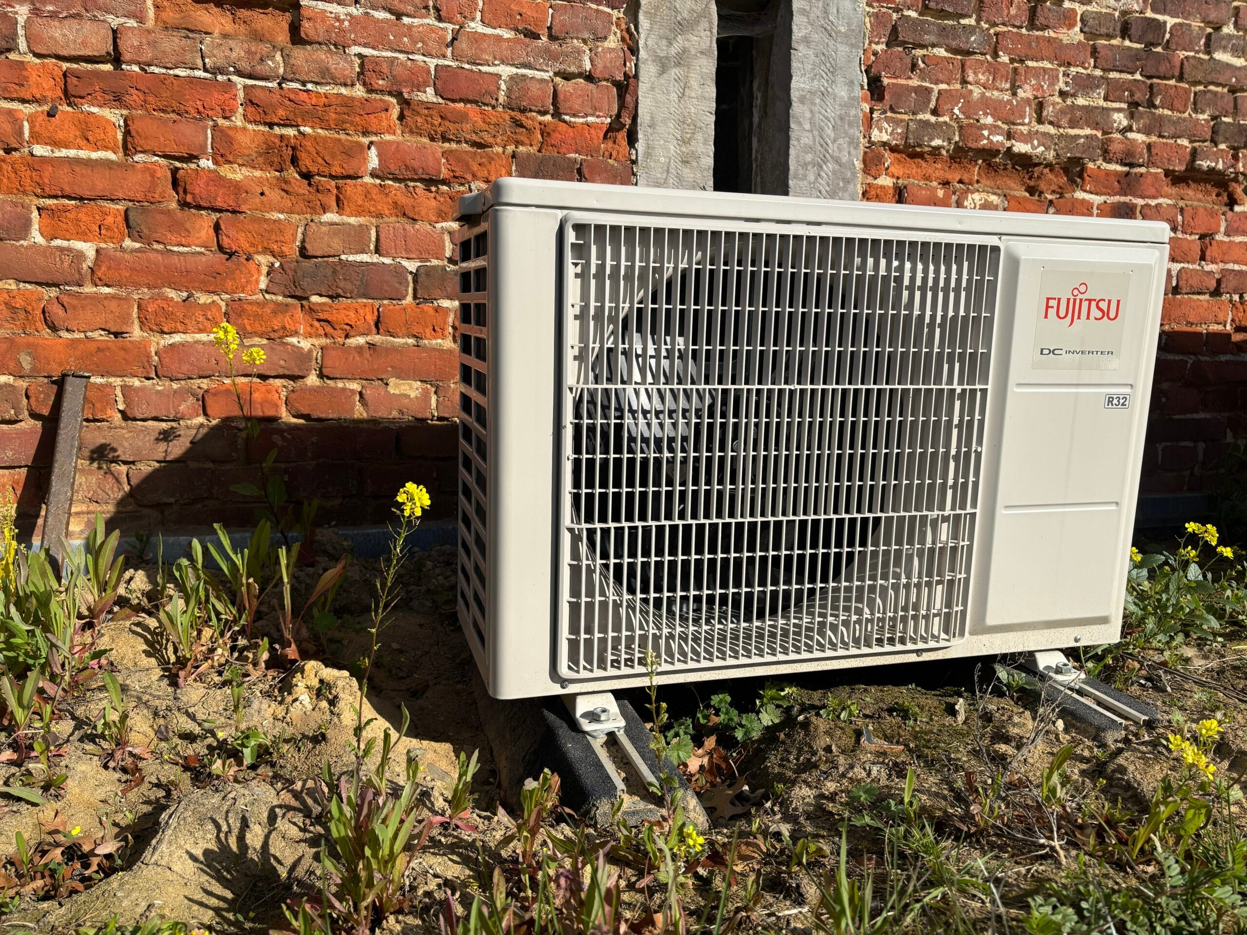 Unité extérieure de climatisation Fujitsu au pied d'une façade en briques à Forville
